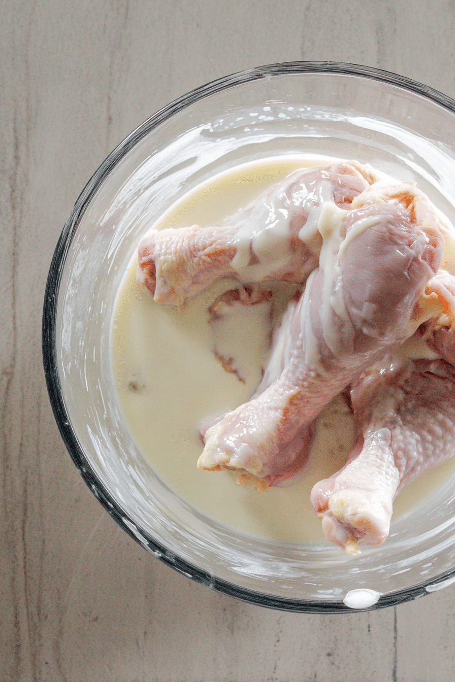 Raw chicken drumsticks marinating in buttermilk in a glass bowl