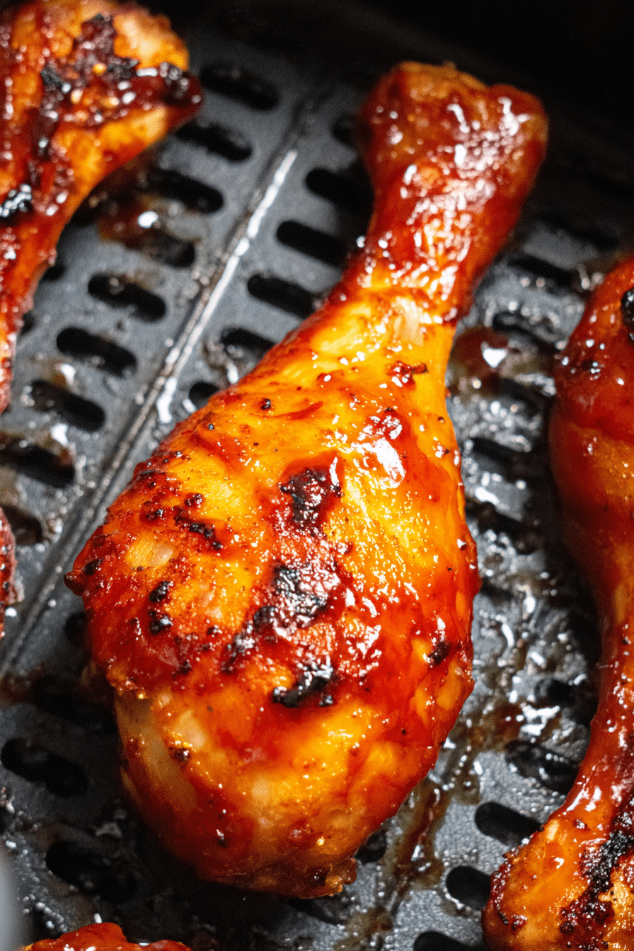 Close-up of a juicy BBQ air fryer chicken drumstick with caramelized sauce in a black air fryer basket.