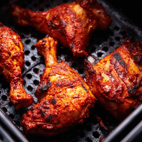 Tandoori-style air fryer chicken leg quarters with crispy charred skin in black air fryer basket