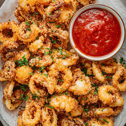 Crispy air fryer calamari rings served with marinara dipping sauce on parchment paper