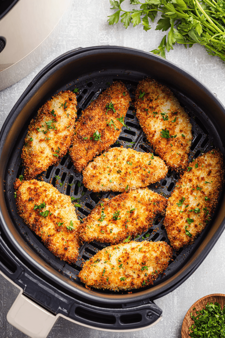 Golden ranch-seasoned chicken tenders cooking in an air fryer basket with fresh parsley garnish