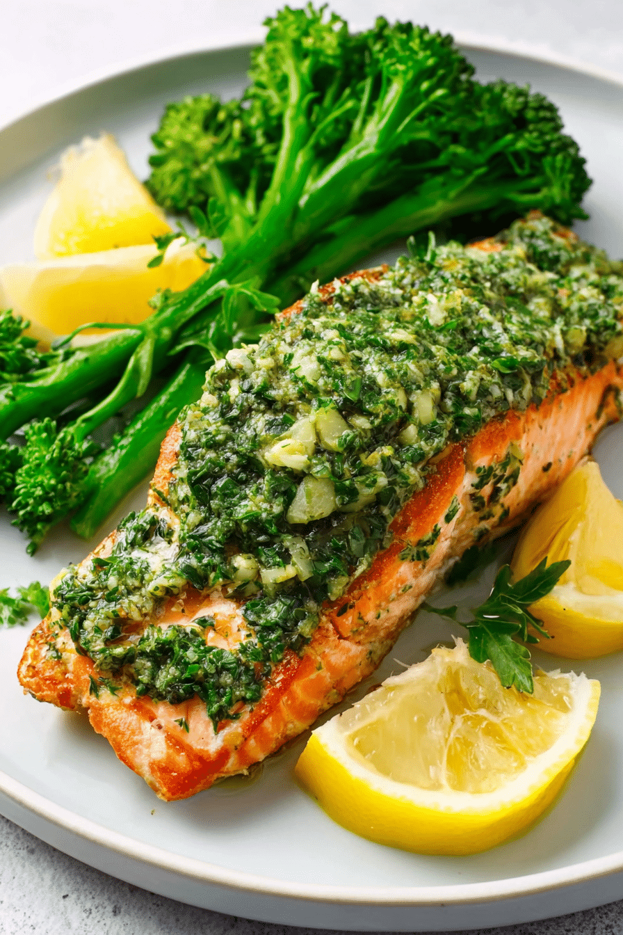Air fryer salmon fillet topped with fresh green chimichurri sauce, served with steamed broccoli and lemon wedges.