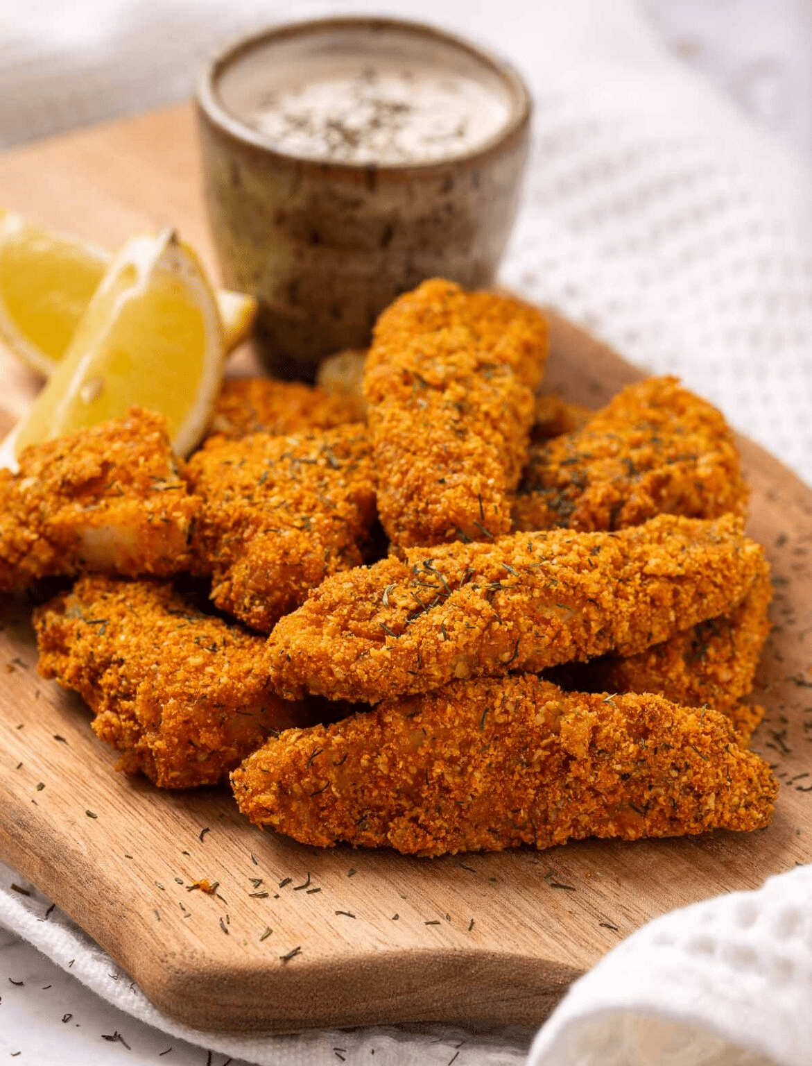 Air fryer keto fish sticks with crispy coating served with creamy dipping sauce and lemon slices on a wooden board