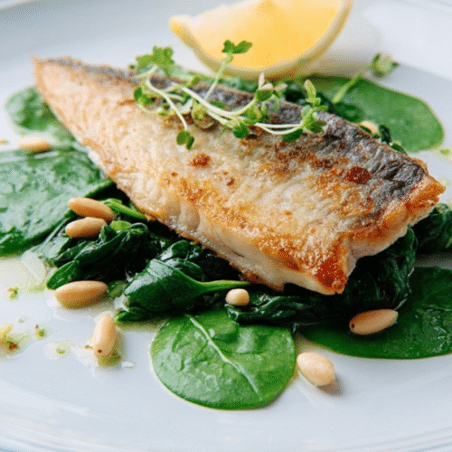 Air fryer mackerel with crispy golden skin served on sautéed spinach and pine nuts with lemon wedge