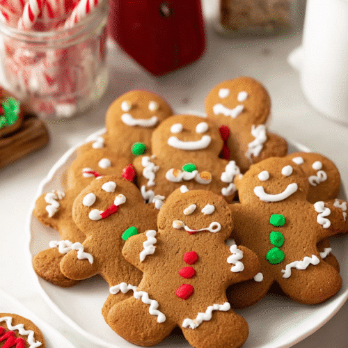 gingerbread cookies decorated with holiday icing on a plate with candy canes nearby