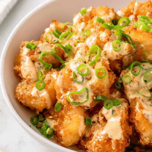 bang bang shrimp with crispy coating and creamy spicy sauce topped with green onions in a white bowl